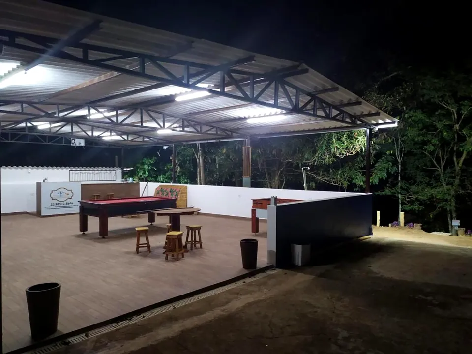 Área de jogos coberta e iluminada à noite, com mesa de sinuca, piso de cerâmica e mata ao fundo