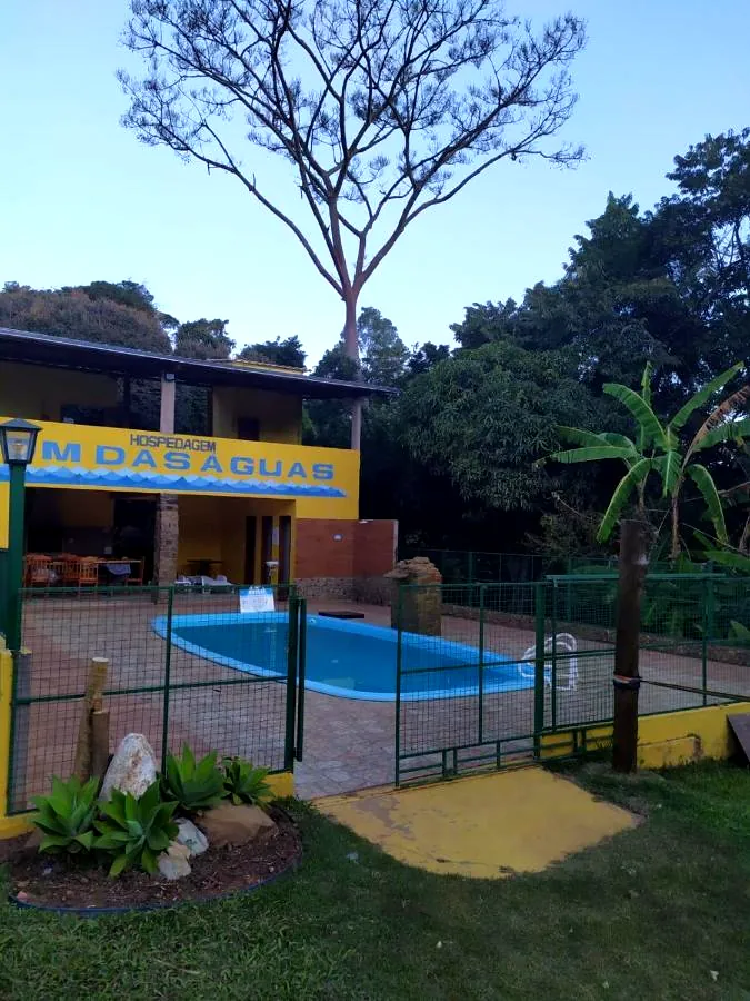 Casa amarela com o letreiro Som das Águas e a piscina cercada em frente