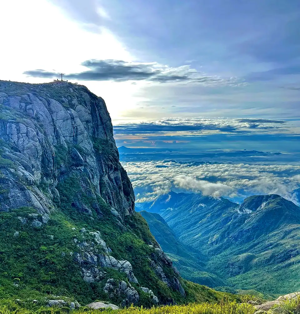 Paredão de pedra do Pico da Bandeira acima de um mar de nuvens e vales verdes