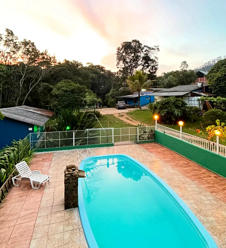 Piscina da hospedagem no fim da tarde, com luzes acesas e céu rosado