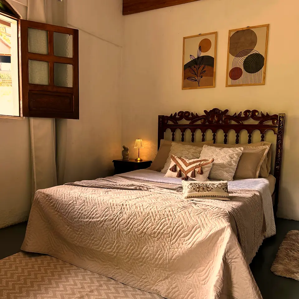 Quarto do chalé com cama de casal de cabeceira entalhada, abajures e quadros com folhas