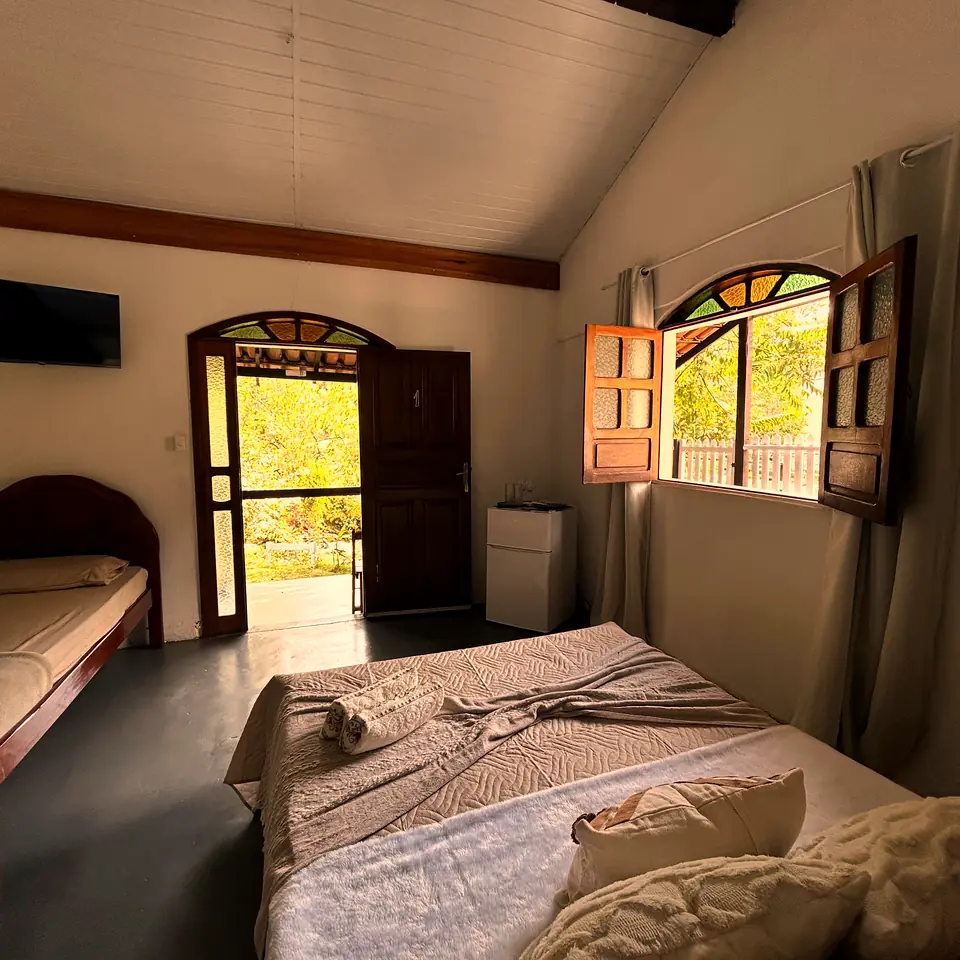 Quarto com janela de madeira aberta para as árvores e cama de solteiro